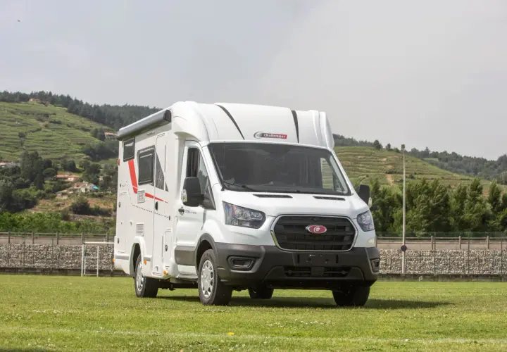 Porteur Ford camping-car blanc, prêt pour l'aventure sur un terrain verdoyant, avec des collines en arrière-plan.