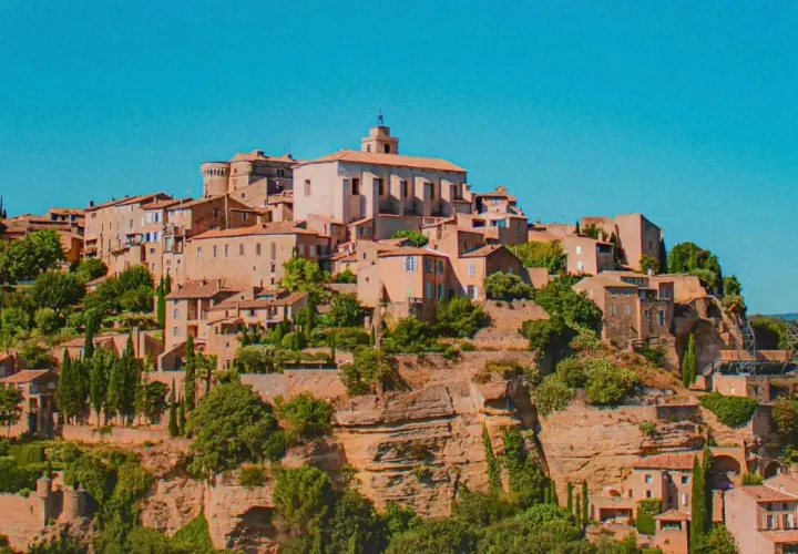 Village perché en Provence, idéal pour un budget vacances. Maisons en pierre, toits de tuiles, végétation luxuriante sous un ciel bleu.