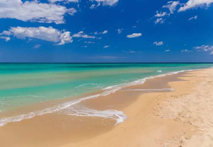 Plage de Bari, sable doré, eaux turquoise et ciel bleu azur avec des nuages blancs. Un rêve d'évasion.