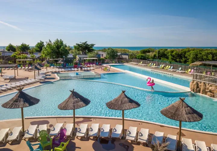 Belle aire camping car à Marseillan avec piscines, transats et parasols. La mer est visible au loin.