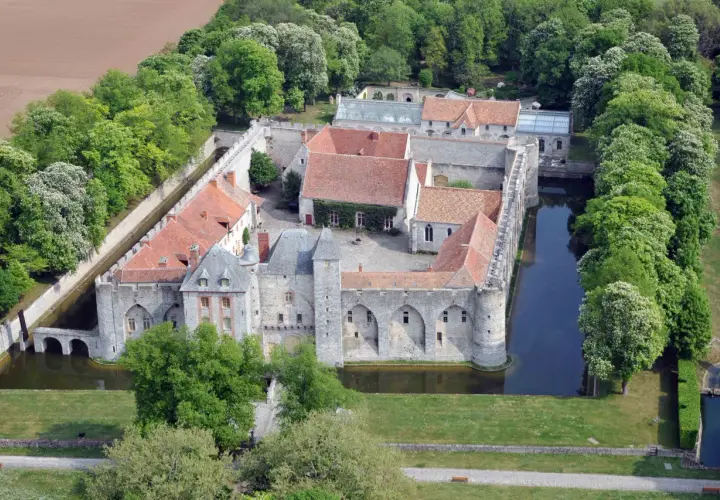 Vue aérienne du **château de Farcheville**, entouré de douves et de verdure. Ses toits de tuiles rouges contrastent avec les murs de pierre grise.