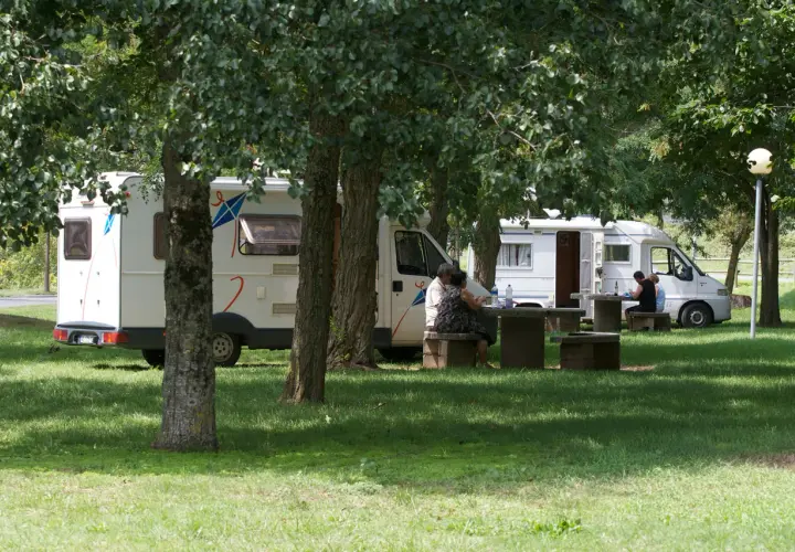 Des camping-cars stationnés dans un parc ombragé, des gens profitent de pique-niques. Un aperçu des plus belles aires de camping-car gratuites.