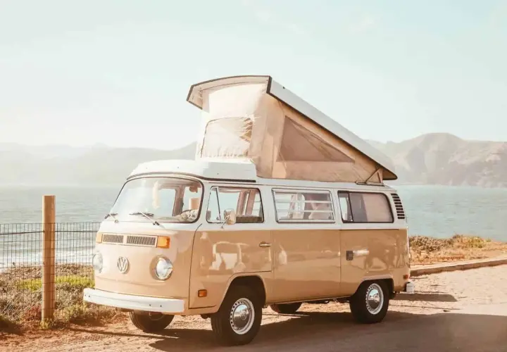 Un camping-car Volkswagen vintage, prêt pour l'aventure, avec son toit relevé, face à la mer et aux collines. L'esprit des 5 Terres en camping-car.