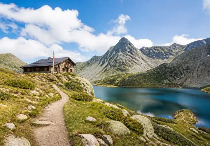 Sentier de randonnée en Andorre menant à un refuge de montagne près d'un lac alpin aux eaux bleues, avec des montagnes escarpées en arrière-plan.