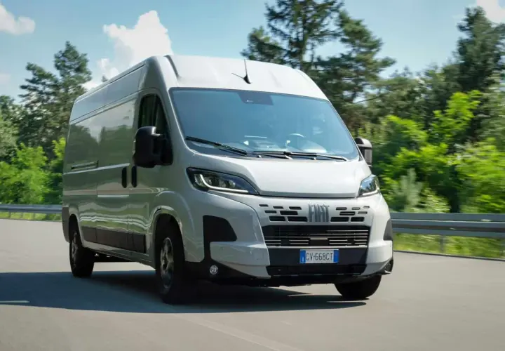 Un Fiat Ducato 2.2 Multijet 140 CV AdBlue blanc roule sur une route bordée d'arbres verts.