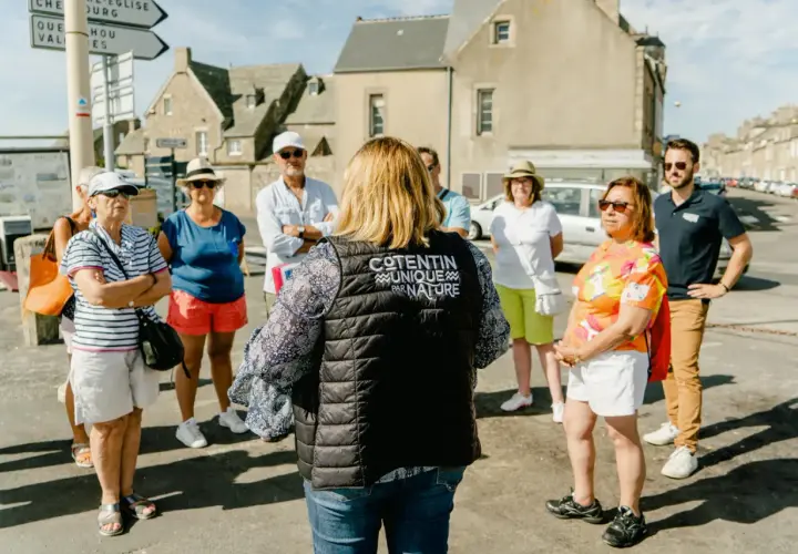 Un groupe de touristes écoute attentivement une guide dans le Val de Saire, un lieu unique par nature.