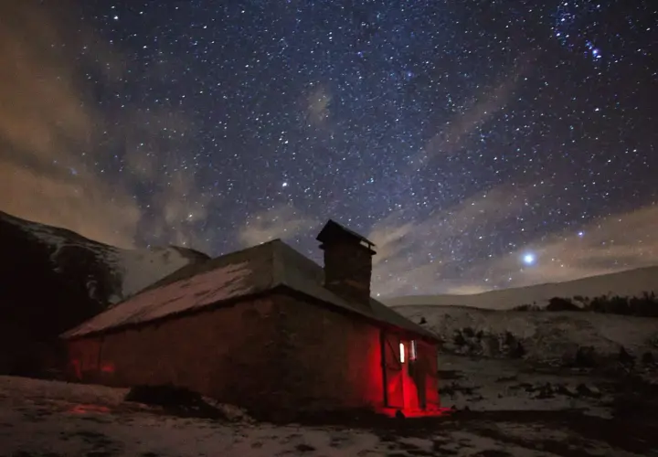 Un refuge illuminé par une lumière rouge sous un ciel étoilé. L'endroit parfait pour dormir en refuge après une longue journée.