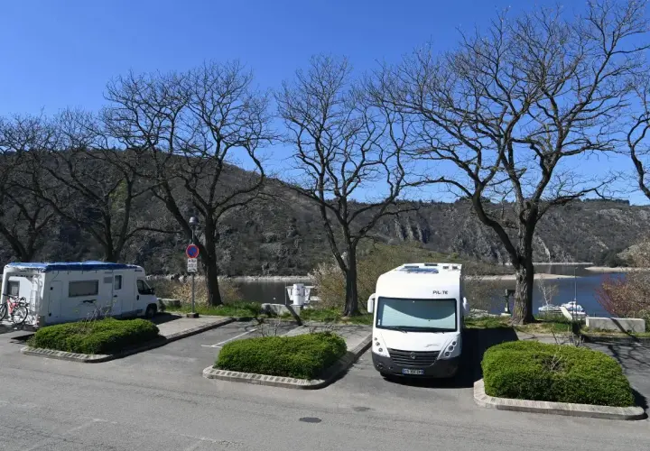 Stationnement pour camping-cars gratuit en Auvergne, avec vue sur le lac et les montagnes. Deux camping-cars sont garés sous des arbres dénudés.