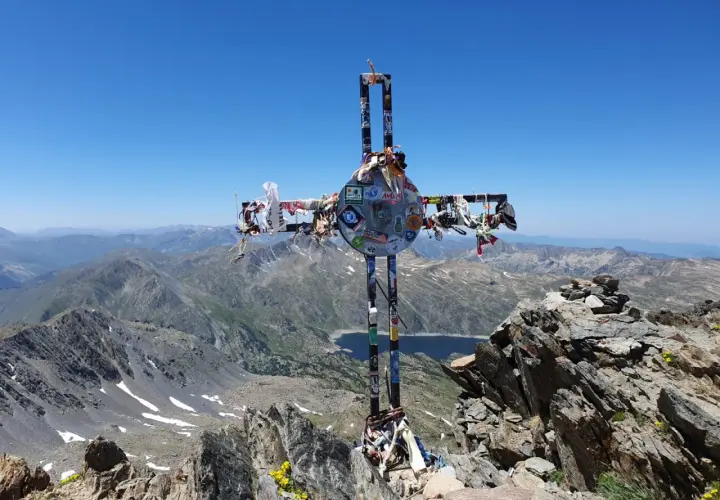 Croix ornée de souvenirs, au sommet d'une montagne, témoin d'un carlit randonnée mémorable. Paysage de haute altitude sous un ciel bleu.