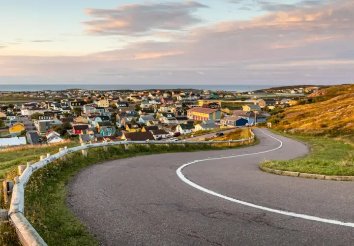 Vue panoramique de Saint-Pierre-et-Miquelon, avec ses maisons colorées nichées sur la côte et une route sinueuse menant au village.