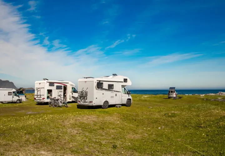 Plusieurs camping-cars stationnés sur une aire de camping car gratuite, face à la mer sous un ciel bleu.