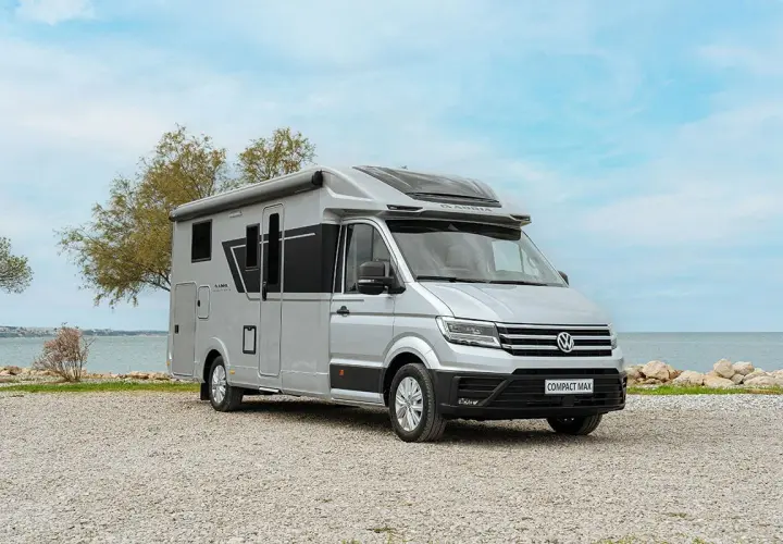Camping car petite taille Adria Compact Max argenté, garé sur un chemin de gravier près de la mer.