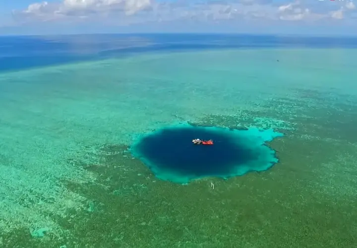 Un bateau rouge et blanc flotte au-dessus du trou du dragon, un abîme bleu profond entouré de récifs coralliens turquoise.