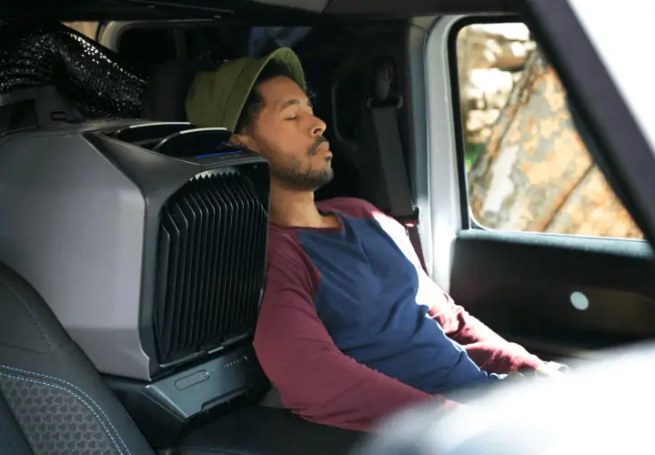 Un homme dort paisiblement dans son camping-car, grâce à un climatiseur portable. L'idéal pour une aire de camping-car gratuit avec électricité.