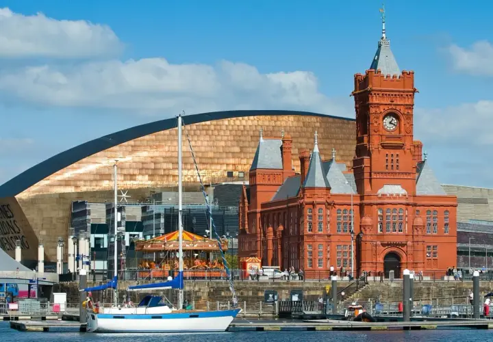Bateaux amarrés dans le port de Cardiff, avec le bâtiment historique en brique rouge et le bâtiment moderne aux écailles cuivrées. Idéal pour visiter Cardiff.