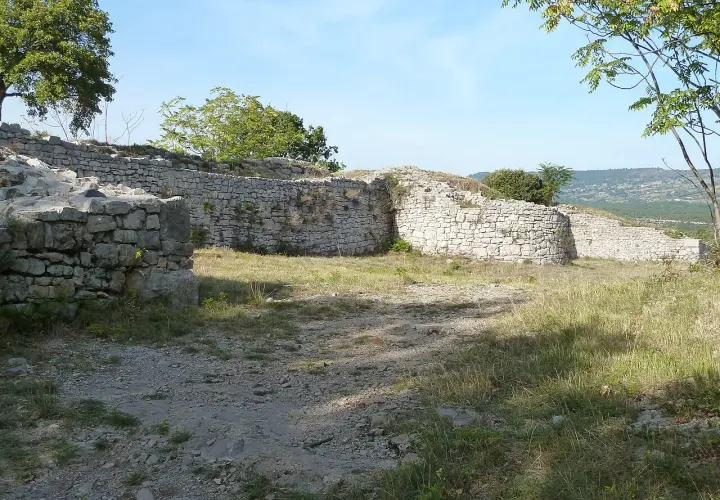 Ruines d'un oppidum gaulois en pierre, avec des murs et des arbres sous un ciel bleu.