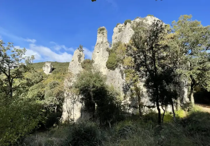 Les Aiguilles de Valbelle, formations rocheuses spectaculaires, se dressent sous un ciel bleu, entourées de verdure.