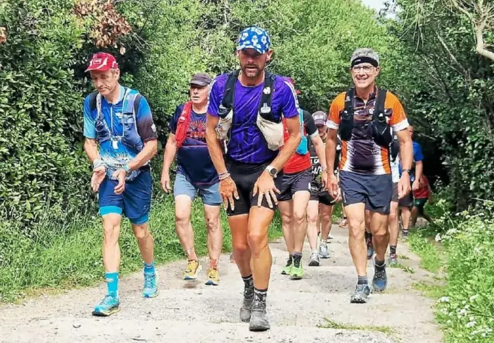 Coureurs en tenue de trail, certains avec des sacs d'hydratation, sur un sentier boisé. Le coureur au centre, portant une casquette bleue, semble en pleine course, peut-être en quête d'un record gr34.