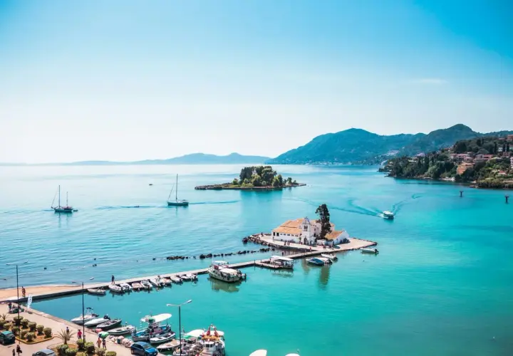 Vue idyllique de la baie de Corfou avec des bateaux, une église sur un îlot et des collines verdoyantes. Idéal pour savoir que faire à Corfou.