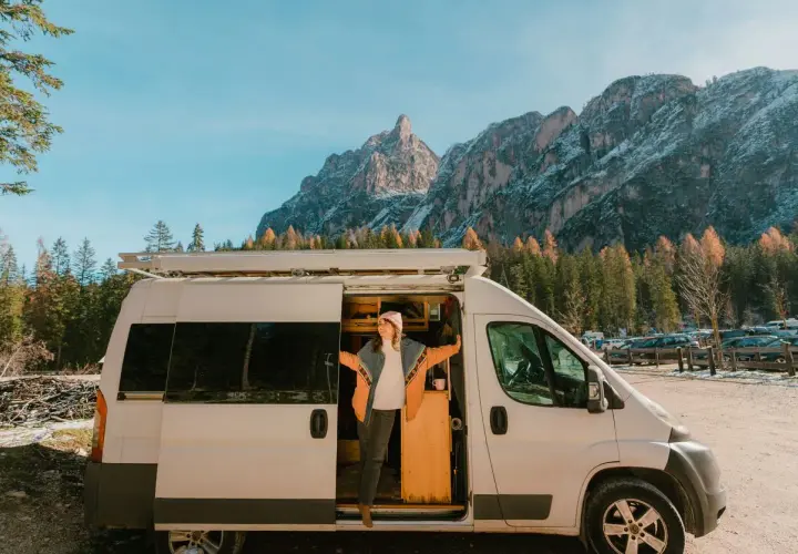 Une femme sort de son fourgon aménagé, profitant d'une vue spectaculaire sur les montagnes. Une image qui pourrait bientôt devenir un souvenir, car les fourgons aménagés vont être interdits.