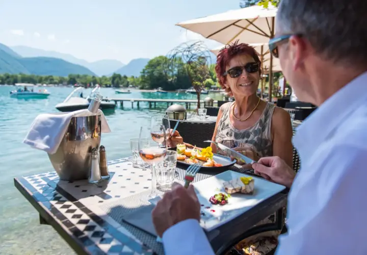 Un couple savoure un repas gastronomique avec vue sur le lac d'Annecy. La plage est magnifique.