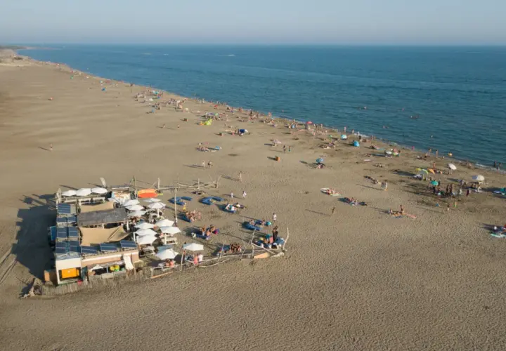 Vue aérienne d'une plage privée au Grau-du-Roi, avec des parasols, des transats et des baigneurs profitant du soleil et de la mer.