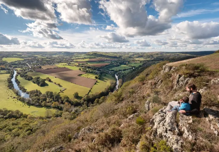 Vue panoramique de la Suisse Normande, une carte vivante de collines verdoyantes, d'une rivière sinueuse et d'un père et son enfant contemplant le paysage.