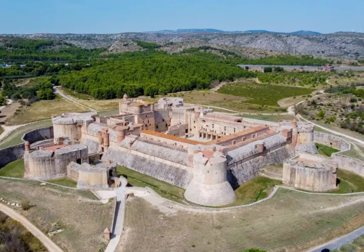 Vue aérienne du Fort de Salses, une imposante citadelle sur la côte vermeille, entourée de verdure et de collines.