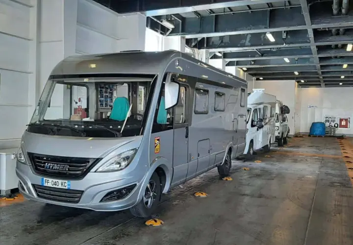 Camping-cars alignés dans la cale d'un ferry, prêts pour la traversée vers la Corse. Le tarif de la traversée pour la Corse en camping-car est affiché sur un panneau.