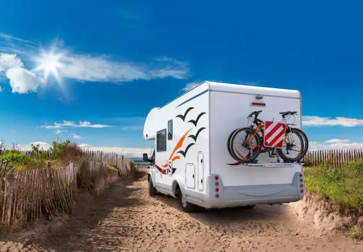 Camping-car prêt pour l'aventure sur une aire de camping car Ile de Ré, avec vélos à l'arrière, sous un ciel bleu éclatant.
