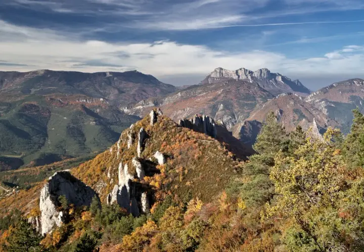 Vue panoramique des gorges de la Roanne en automne. Un sentier de randonnée serpente à travers des crêtes rocheuses et des forêts aux couleurs flamboyantes.