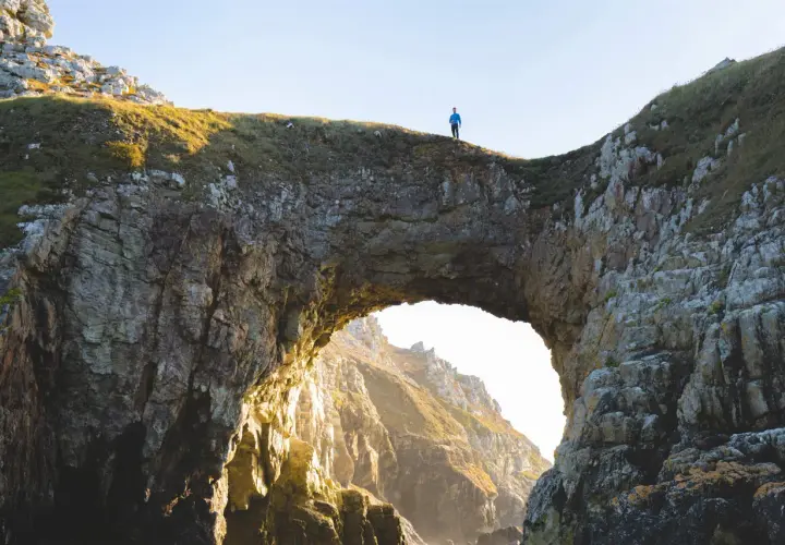 Un homme seul au sommet de la pointe de Dinan, surplombant un arc rocheux naturel.