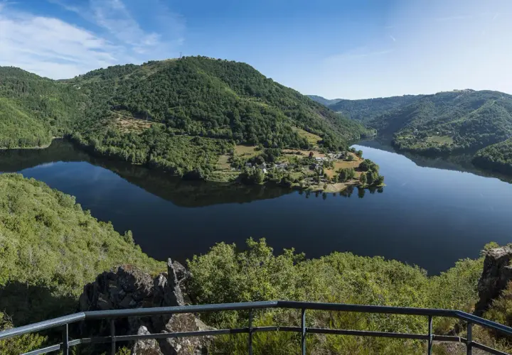 Vue panoramique des gorges de la Truyère, avec un lac paisible reflétant les collines verdoyantes et un village pittoresque.