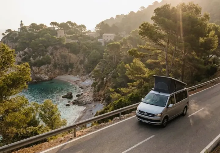 Un camping-car explore les routes sinueuses de la Costa Brava, offrant une vue imprenable sur une crique isolée et un phare au loin.