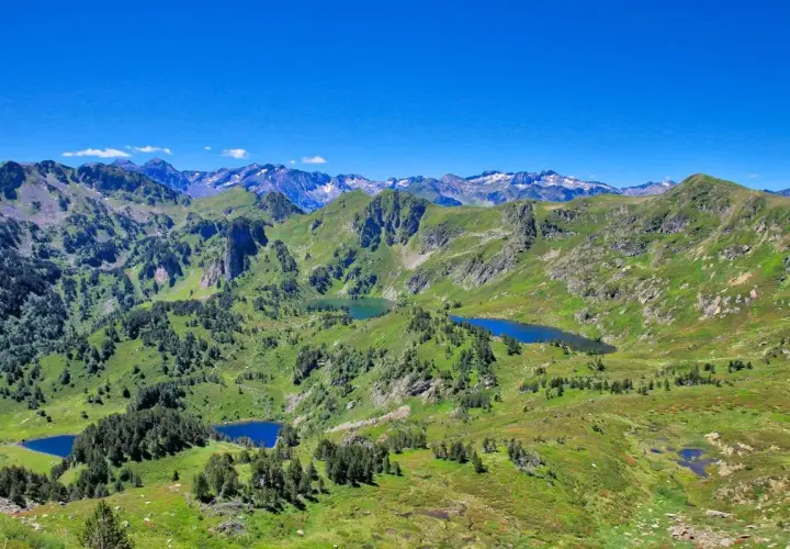Vue panoramique sur les Pyrénées avec plusieurs étangs bleus, dont l'étang de Rabassoles, nichés dans des vallées verdoyantes sous un ciel bleu intense.