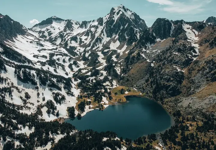 Vue aérienne du lac du Laurenti, niché au pied de montagnes enneigées et de forêts de pins. Un paysage alpin spectaculaire.