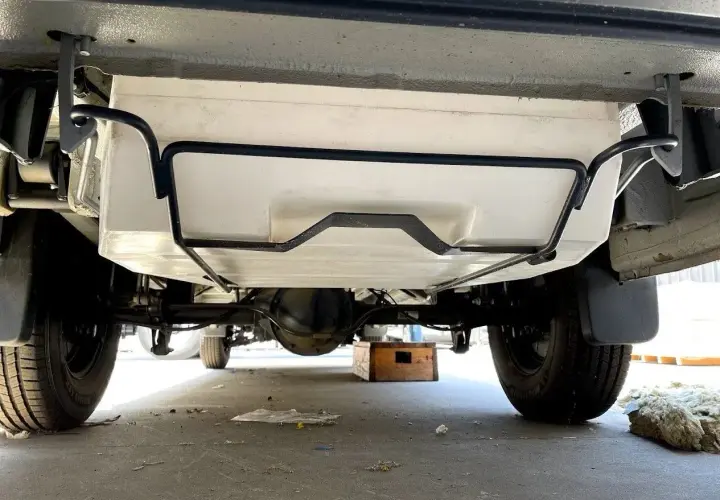 Vue sous un camping-car, montrant le réservoir d'eau propre fixé au châssis. Préparation pour le nettoyage de la cuve camping car.
