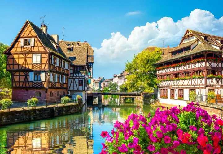 La Petite France à Strasbourg, un joyau pour l'alsace tourisme. Maisons à colombages pittoresques au bord de l'eau, reflets dans le canal, fleurs éclatantes.