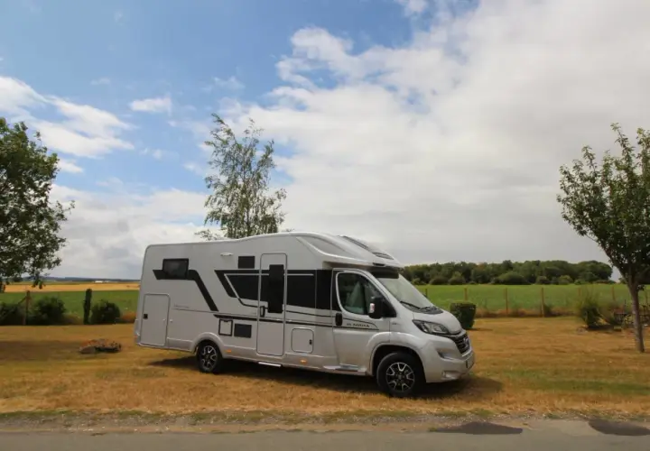 Camping-car Adria Matrix 670 SC argenté, stationné dans un champ sous un ciel nuageux.