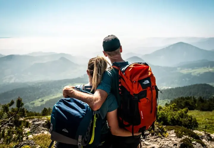 Couple en randonnée, admirant le panorama des montagnes de la Grande Ardèche. Sacs à dos orange et bleus, vue imprenable.
