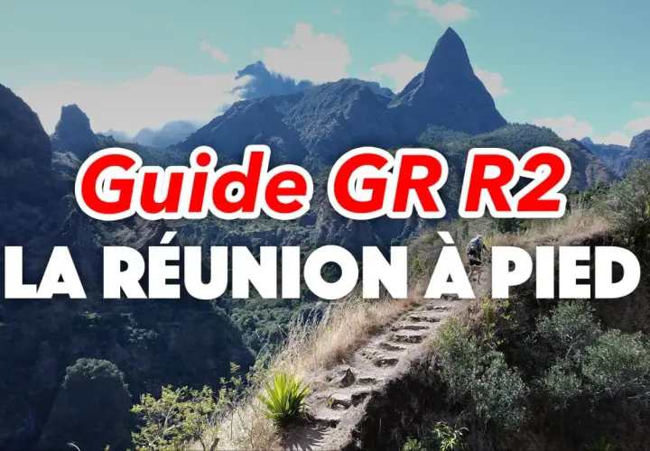 Guide GR R2 : La Réunion à pied, un randonneur sur un sentier escarpé avec des montagnes majestueuses en arrière-plan.