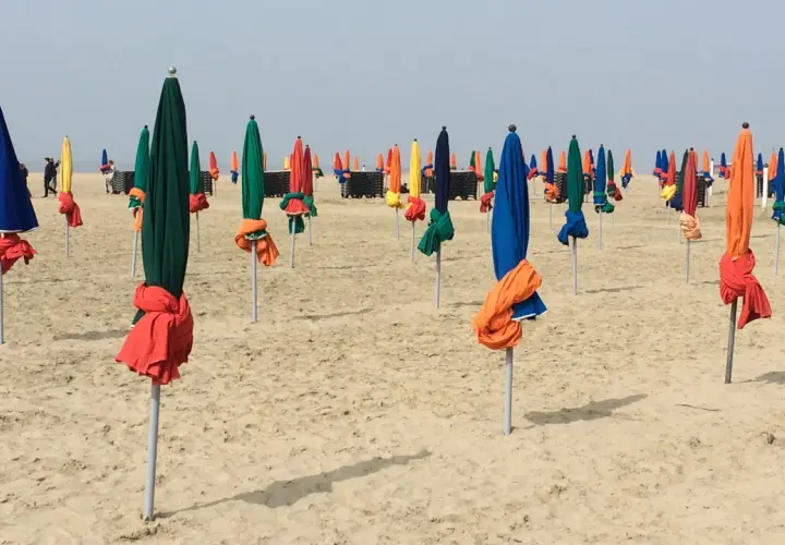 Des parasols colorés, bleus, verts, rouges et jaunes, sont alignés sur la plage de Deauville, prêts à accueillir les visiteurs.