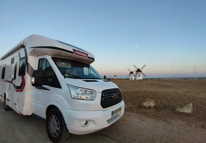 Un camping-car blanc est garé devant des moulins à vent au coucher du soleil. Un voyage en camping-car inoubliable.