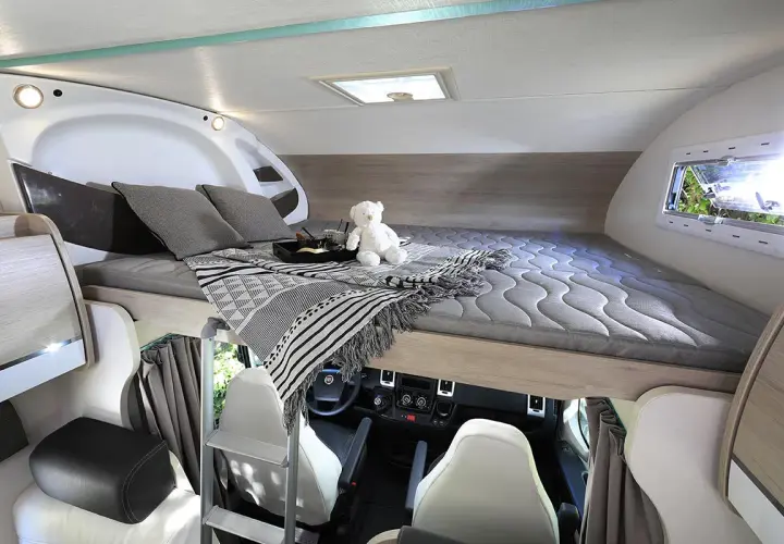 Lit pavillon confortable dans un camping-car, prêt pour une nuit paisible. Un ours en peluche veille sur le sommeil.