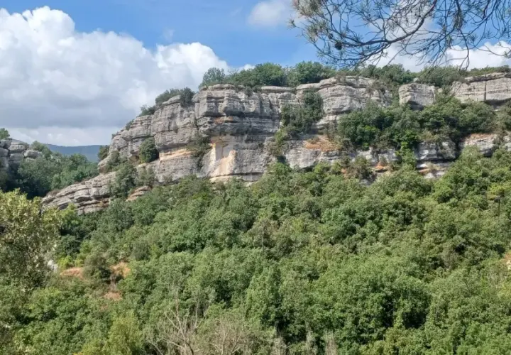 Falaises calcaires spectaculaires des gorges du Caramy, couvertes de végétation luxuriante sous un ciel bleu et nuageux.