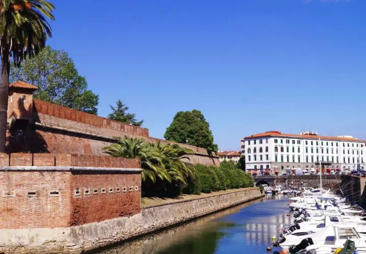Canal bordé de bateaux à Livourne, Italie, avec une ancienne muraille de briques et des palmiers.