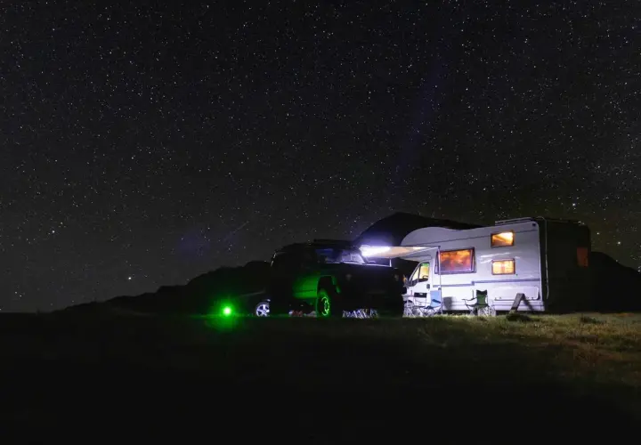 Un camping-car et un 4x4 illuminés sous un ciel étoilé. L'endroit parfait où dormir en camping-car pour admirer la voie lactée.