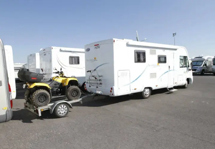 Un quad jaune sur une remorque, prêt à être tracté par un camping-car. Le quad est bien attaché, prêt pour l'aventure, comme indiqué sur la carte grise.