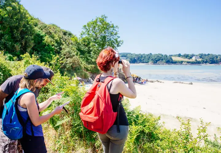 Couple en randonnée à Saint-Jacut-de-la-Mer, consultant une carte. Une femme observe la baie avec des jumelles.