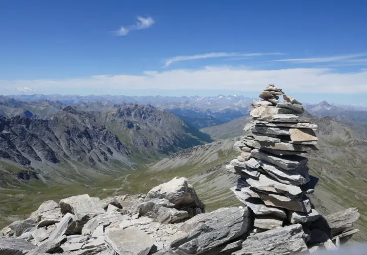 Un cairn, tel un tour du pain de sucre, domine un paysage de montagnes majestueuses sous un ciel bleu.